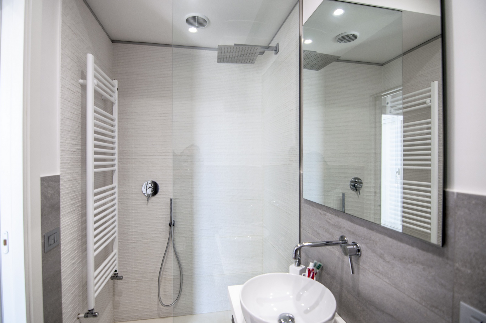 Bagno con doccia in vetro e rivestimenti grigi